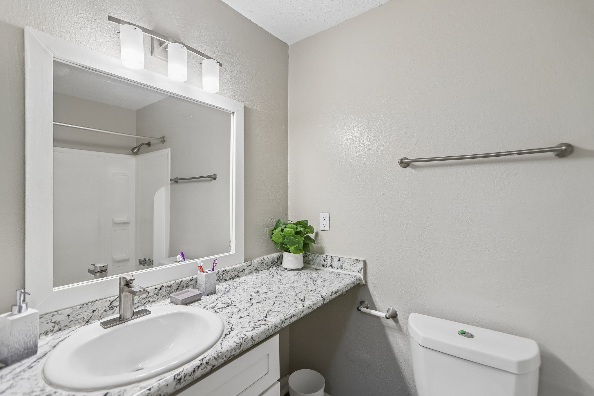 A bathroom with a sink, mirror, toilet and a towel bar.